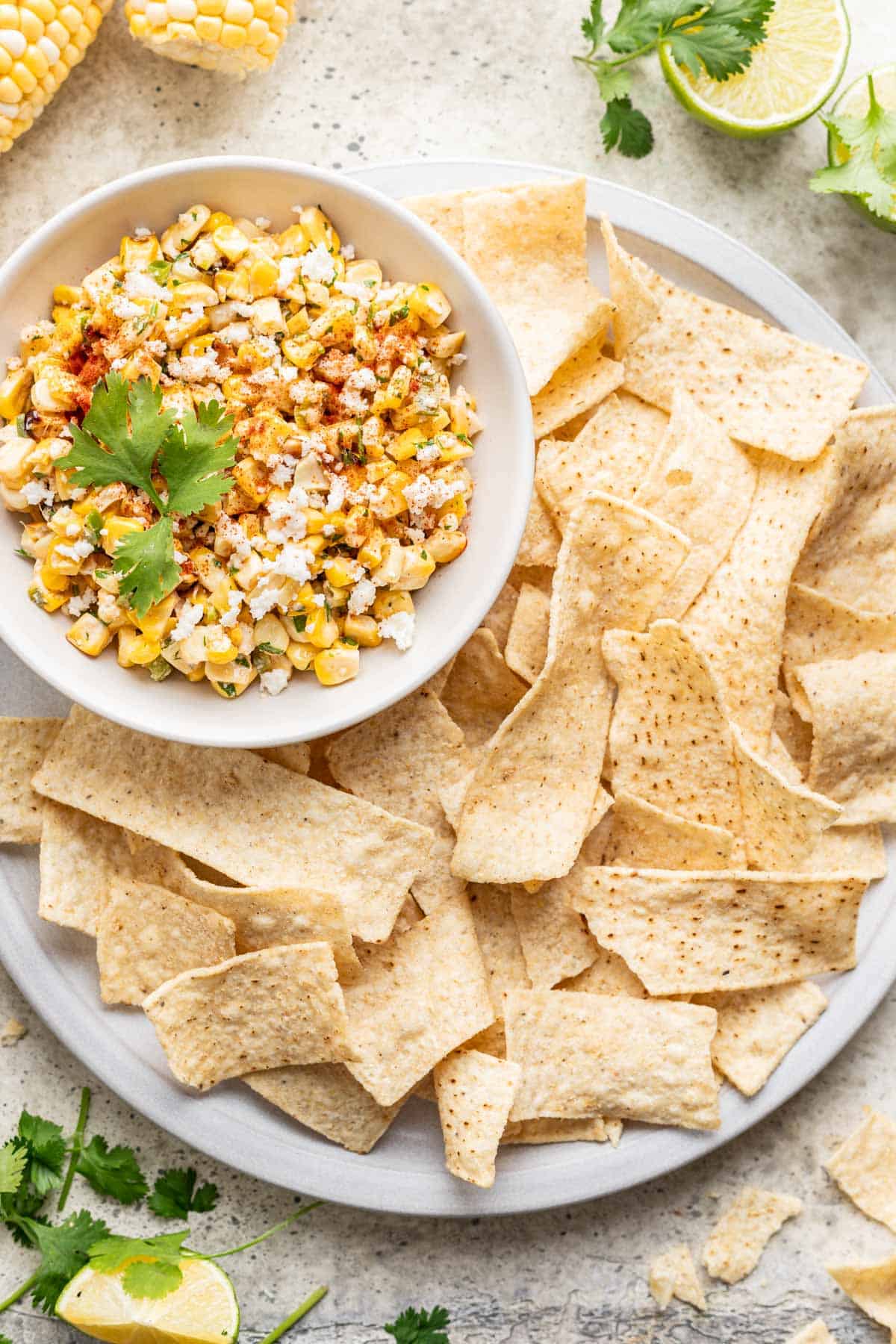 Street corn salsa in a small bowl with tortilla chips on a plate around it.