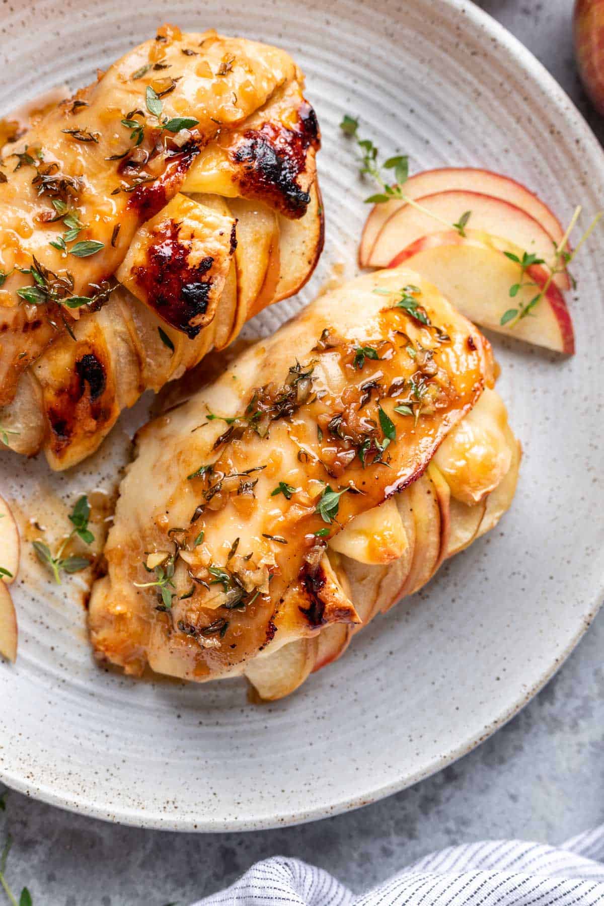 Apple and brie stuffed chicken on a serving plate with sliced apples and fresh thyme.