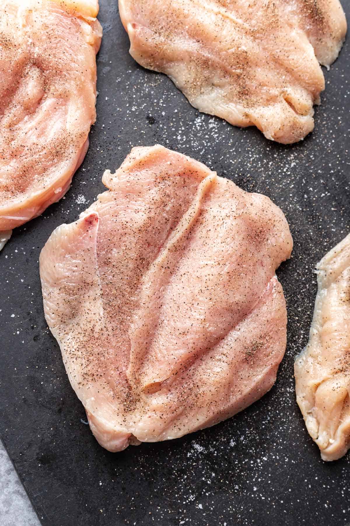 Butterflied chicken breasts on a cutting board, seasoned with salt and pepper.