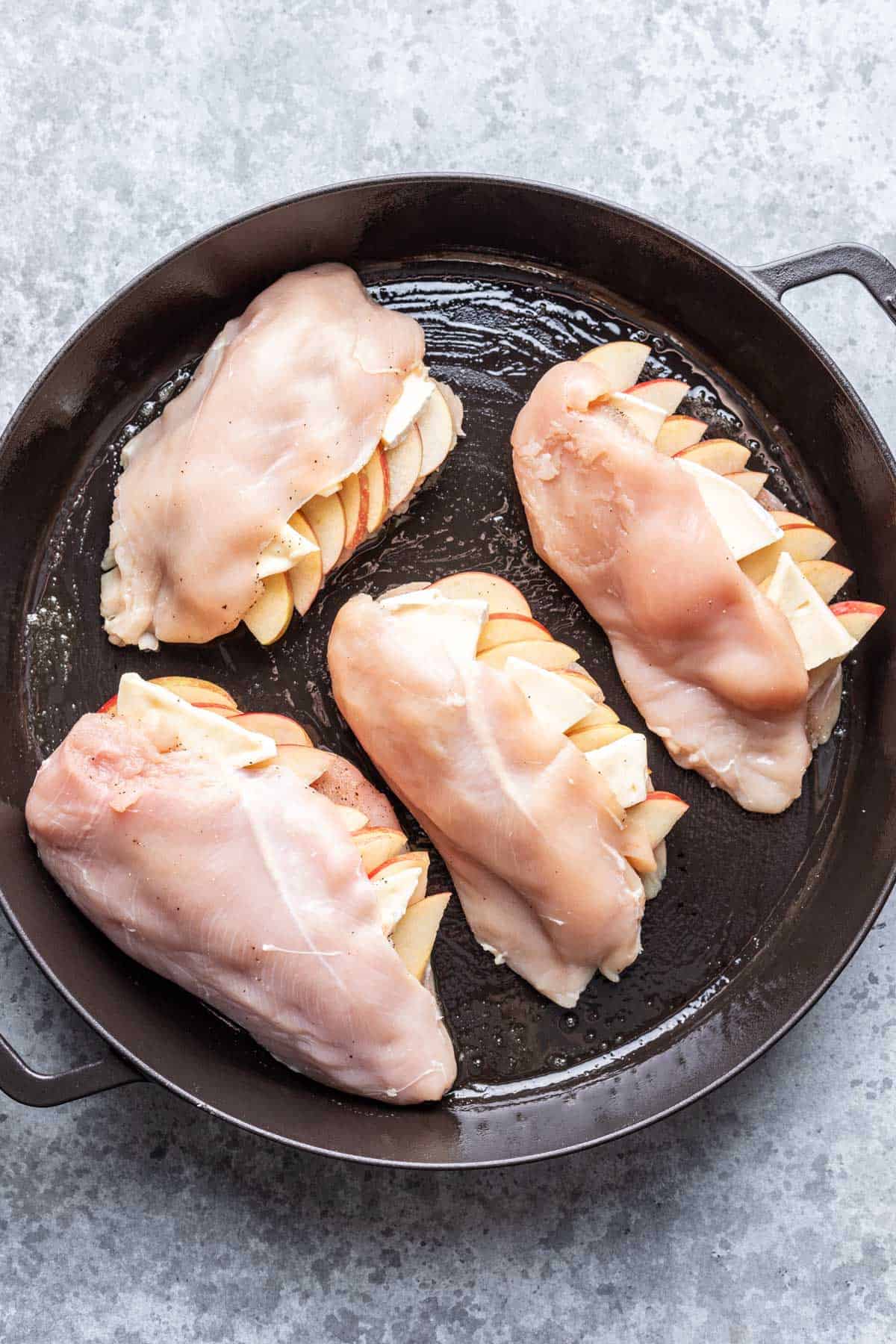 Raw apple and brie stuffed chicken breasts in a cast iron skillet.