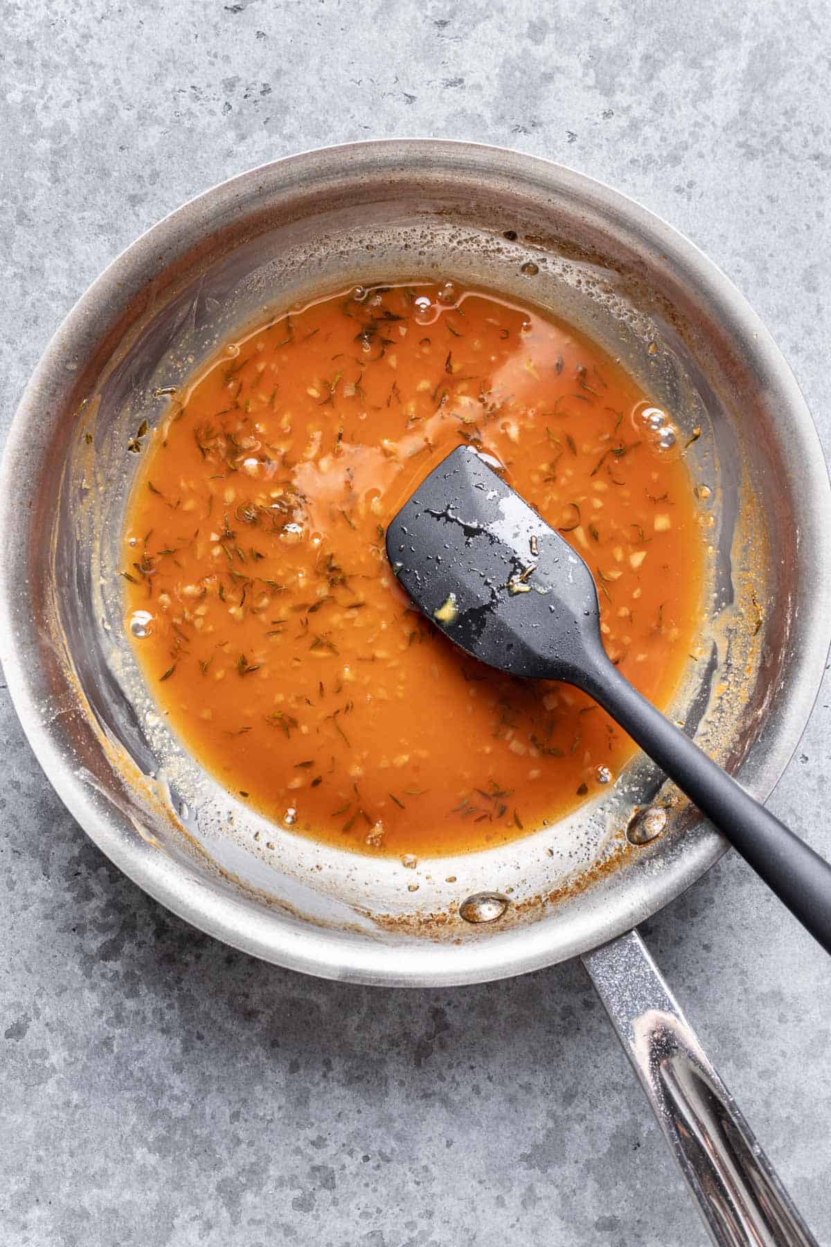 Apple cider and thyme glaze reduced in a skillet.