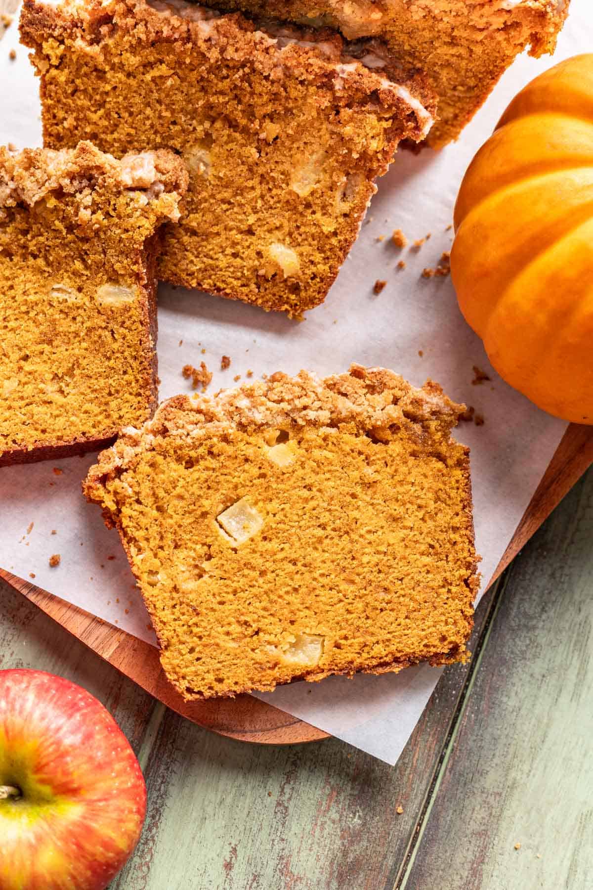 Sliced apple pumpkin bread on a cutting board with a pumpkin on the side.