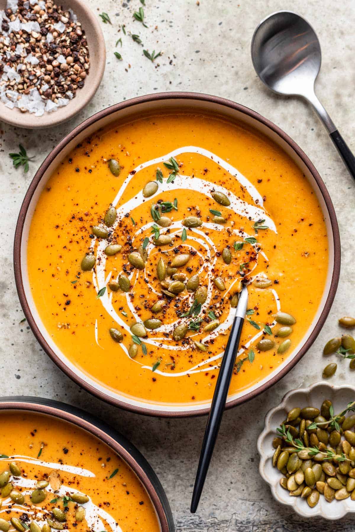 Butternut squash and carrot soup in a black bowl with a soup spoon.