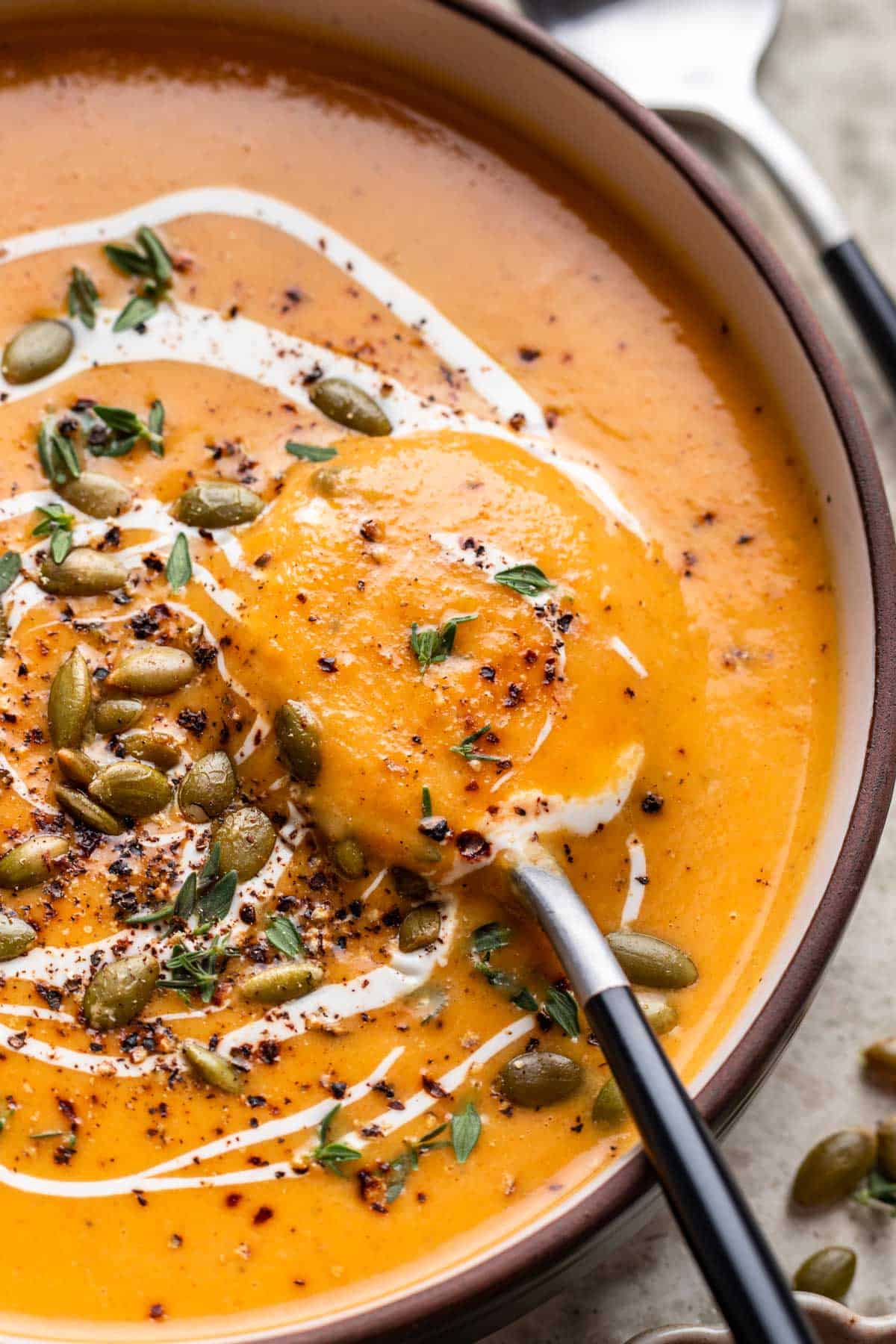 Butternut squash and carrot soup with a soup spoon scooping some out of a bowl.