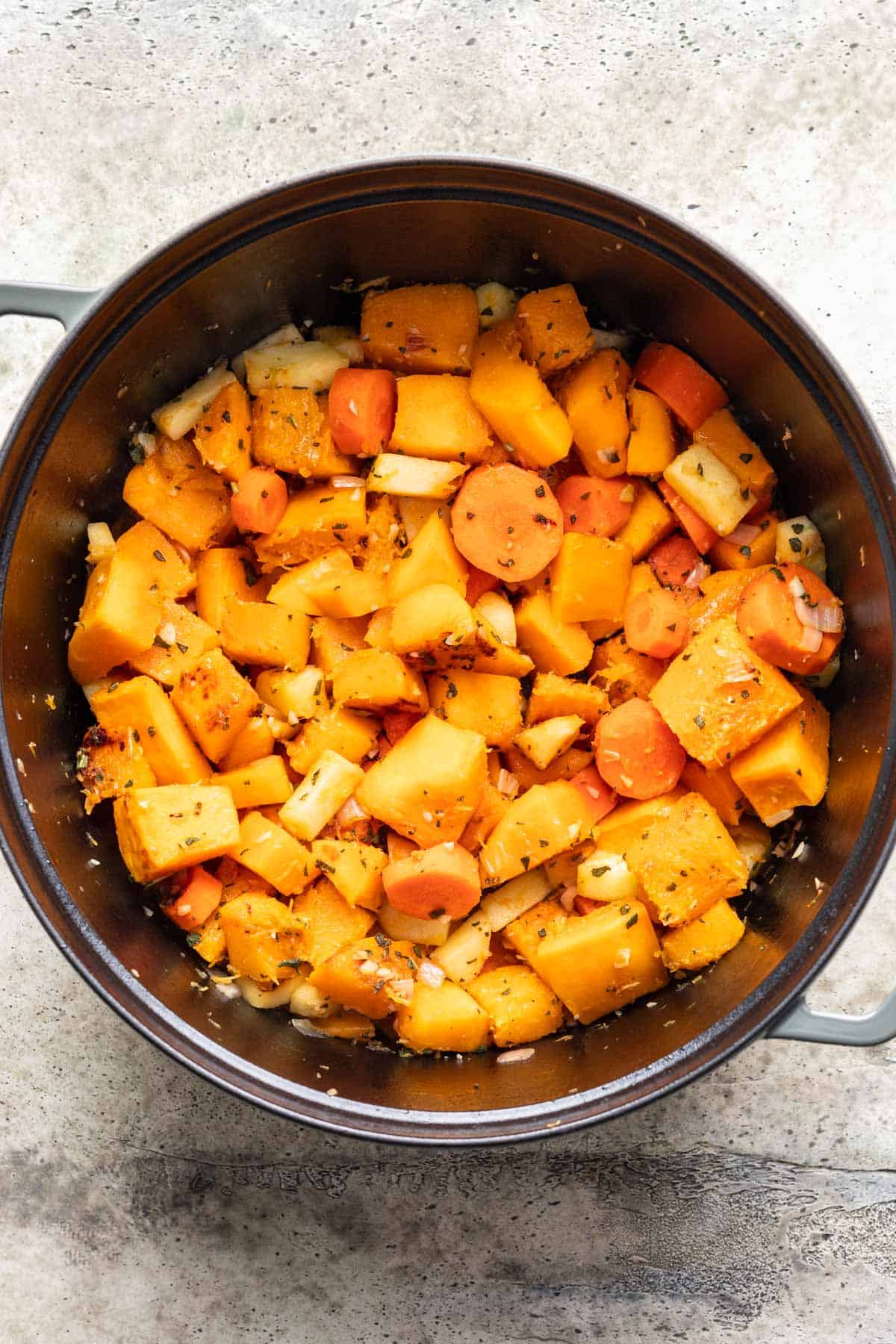 Butternut squash, carrots, shallot, apple, garlic, and sage cooking in a pot.