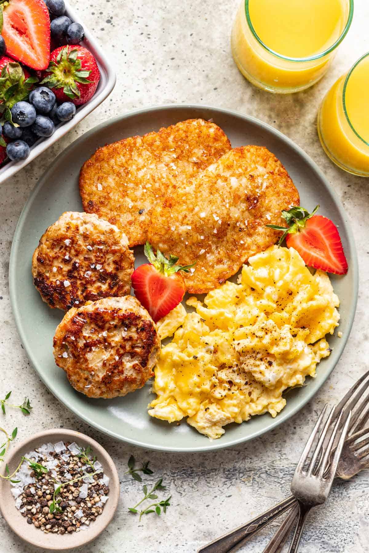 Chicken and apple breakfast sausage on a plate with scrambled eggs and hashbrowns.