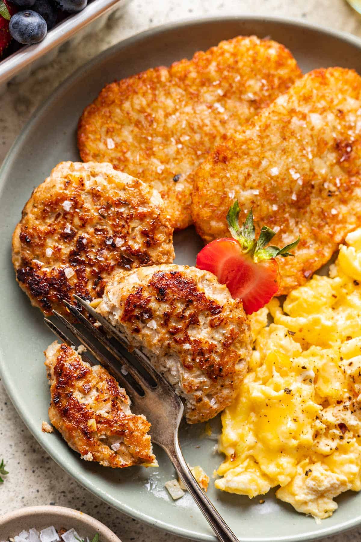 Chicken and apple breakfast sausage on a plate with a fork cutting it in half.