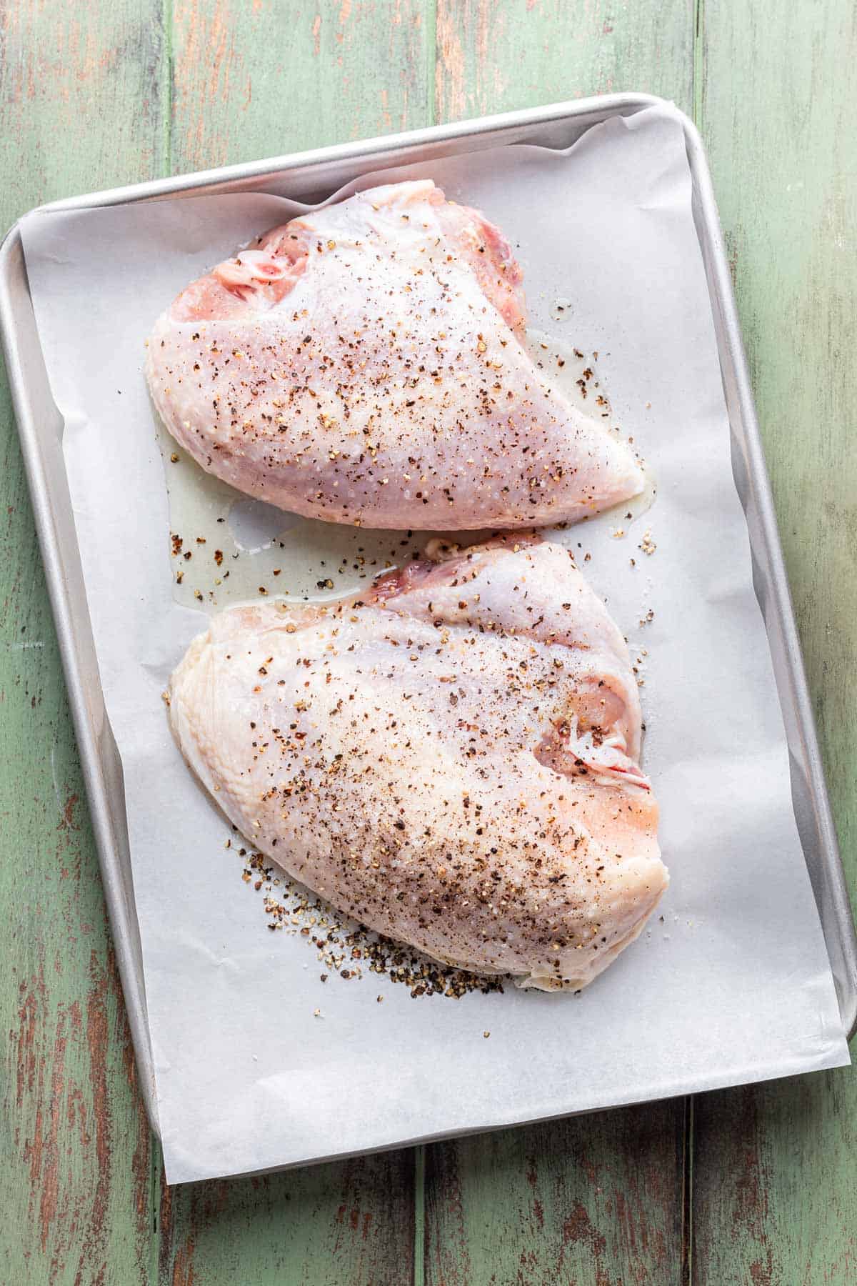 Chicken breasts on a baking sheet seasoned with oil, salt, and pepper.
