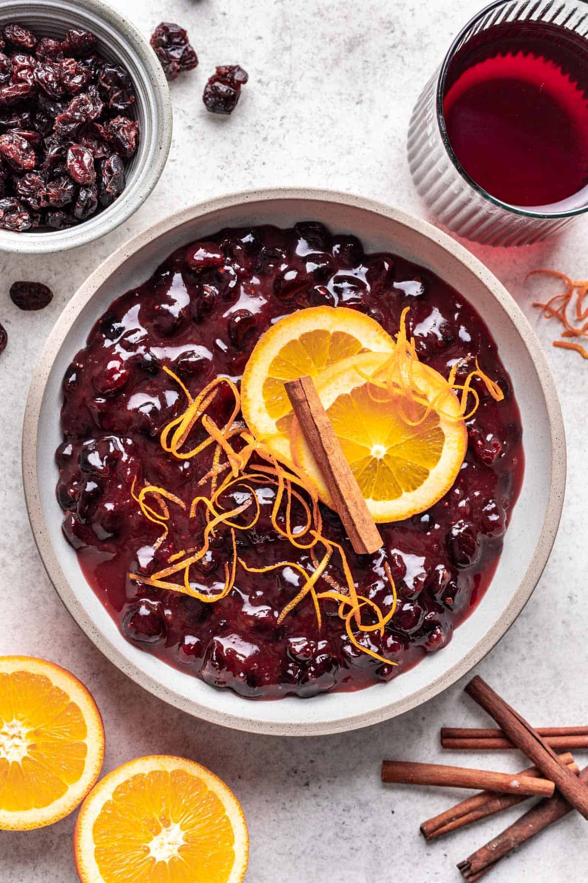Cranberry sauce with dried cranberries in a serving bowl, garnished with sliced oranges, orange zest, and cinnamon stick.