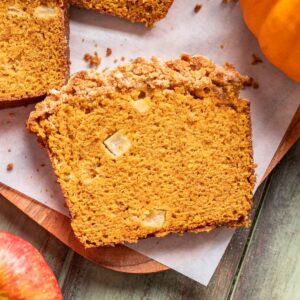 A slice of apple pumpkin bread on a wood cutting board.