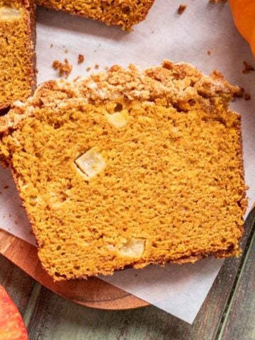 A slice of apple pumpkin bread on a wood cutting board.