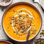 Butternut squash and carrot soup in a bowl topped with cream, pumpkin seeds, and cracked black pepper.