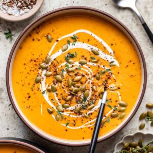 Butternut squash and carrot soup in a bowl topped with cream, pumpkin seeds, and cracked black pepper.