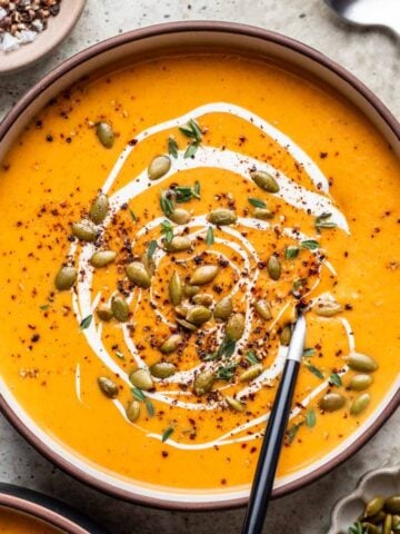 Butternut squash and carrot soup in a bowl topped with cream, pumpkin seeds, and cracked black pepper.