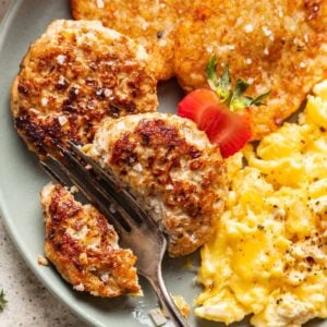 Chicken and apple breakfast sausage on a plate with a fork cutting it in half.