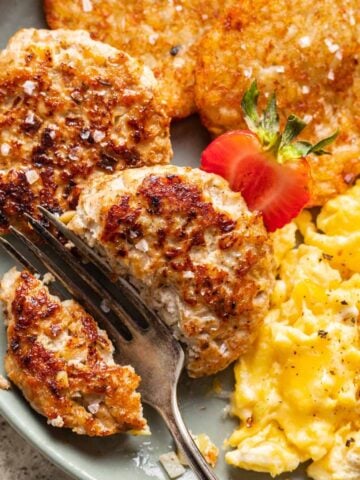 Chicken and apple breakfast sausage on a plate with a fork cutting it in half.