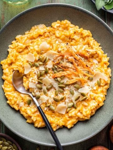 Chicken and Pumpkin Risotto in a green bowl topped with pepitas and shaved parmesan cheese.