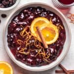 Cranberry sauce with dried cranberries in a bowl, topped with sliced oranges and a cinnamon stick.