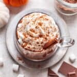 Pumpkin spice hot chocolate in a glass mug with whipped cream on top.