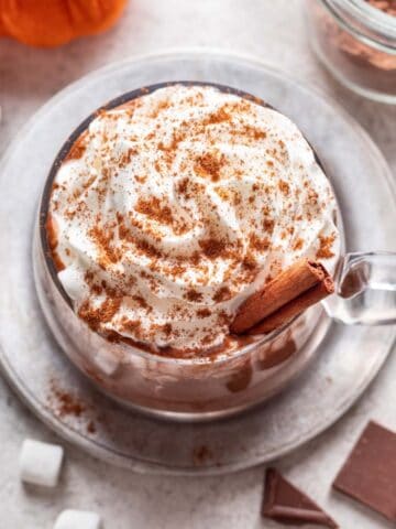 Pumpkin spice hot chocolate in a glass mug with whipped cream on top.