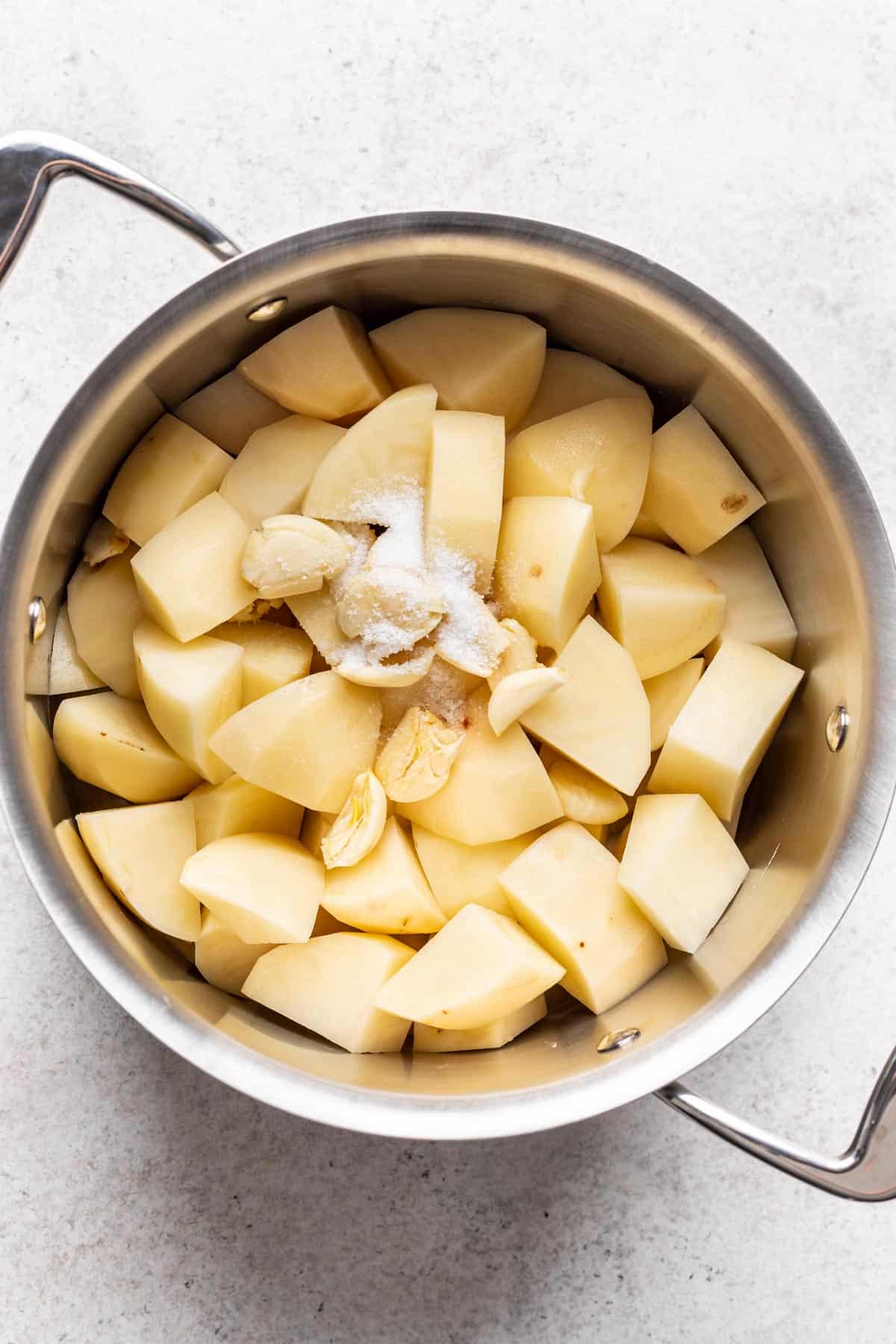 Peeled, diced potatoes in a pot with garlic and salt.