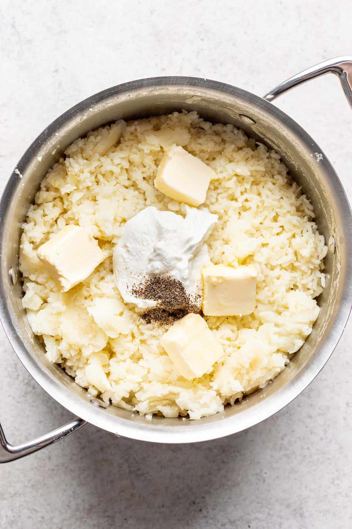Greek yogurt, butter, salt, and pepper added to the riced potatoes in the pot.