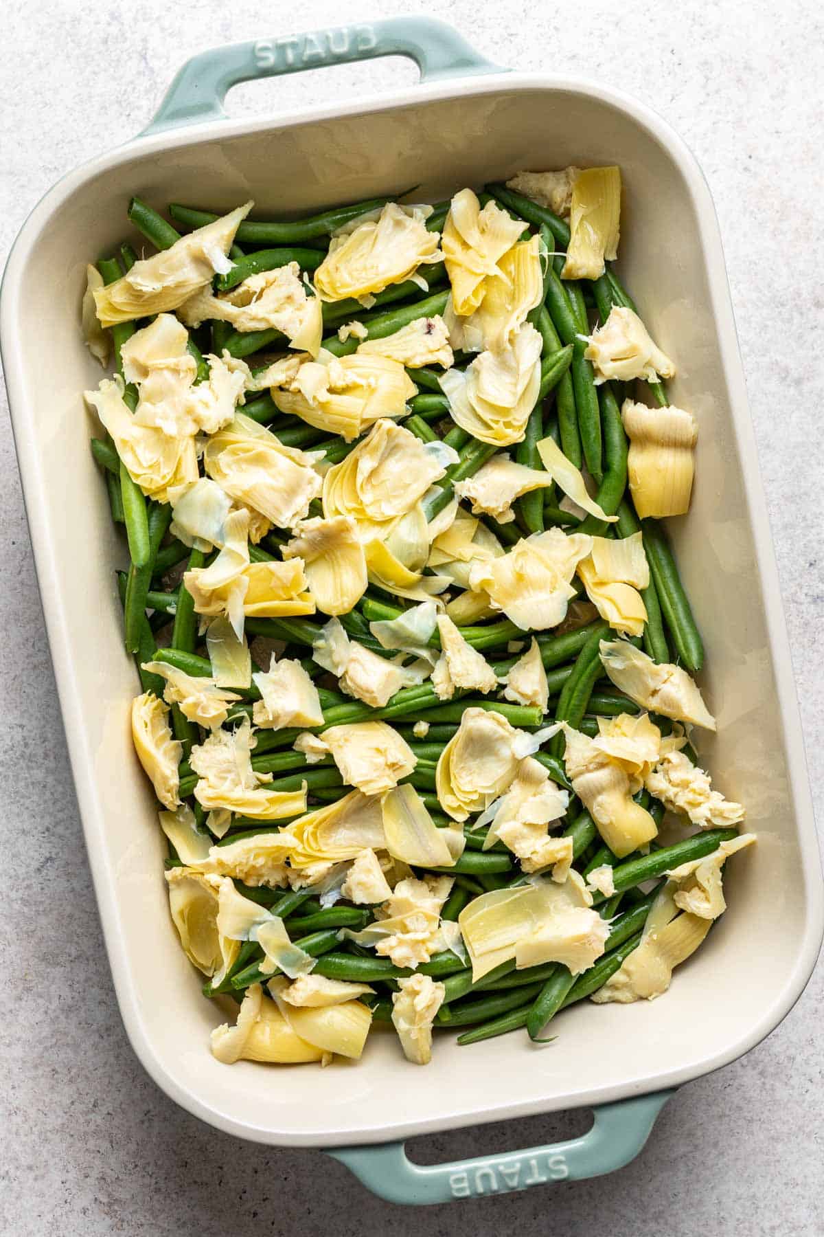 Half of the green beans and artichokes added to a baking dish.