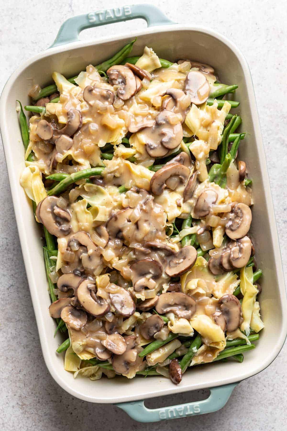 Green beans, artichokes, and mushroom sauce arranged in a baking dish.