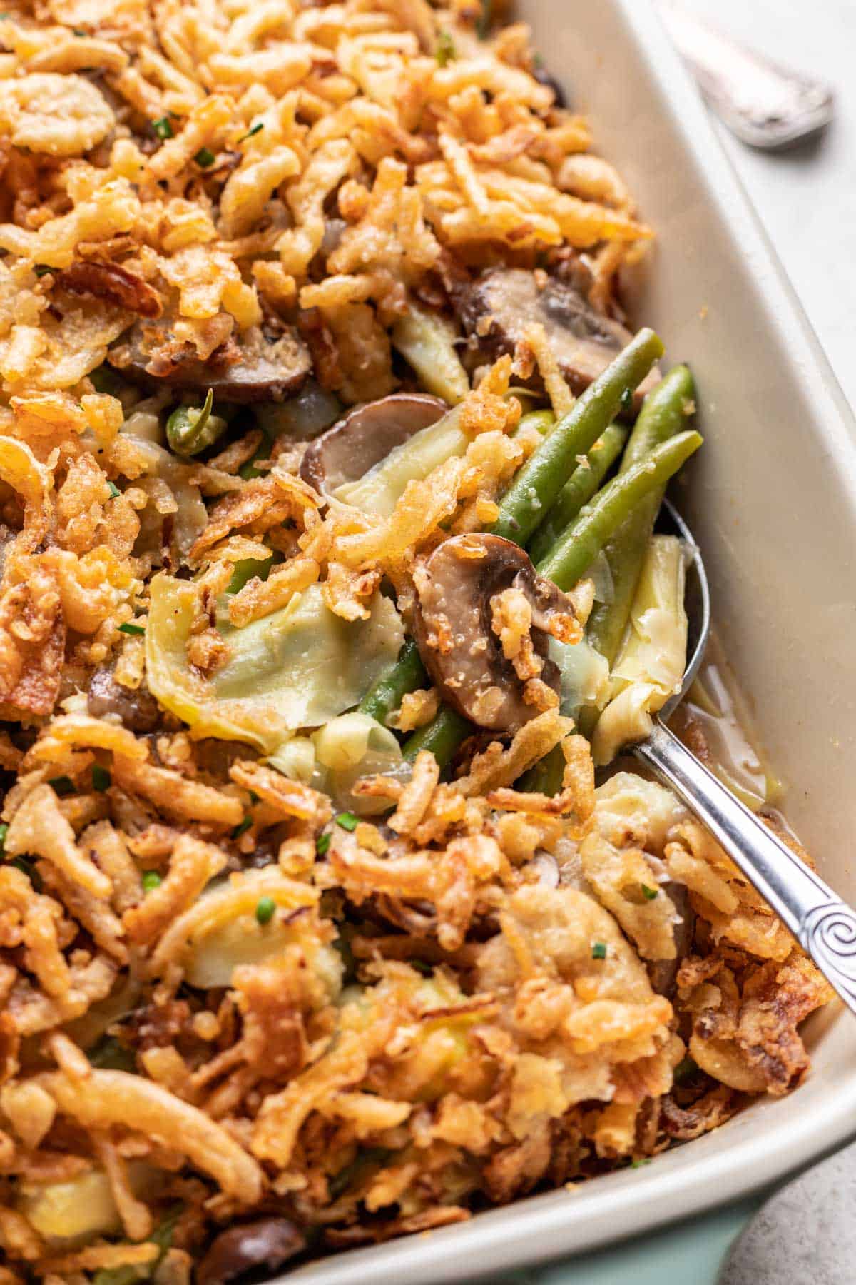 A spoon scooping green bean and artichoke casserole from a baking dish.