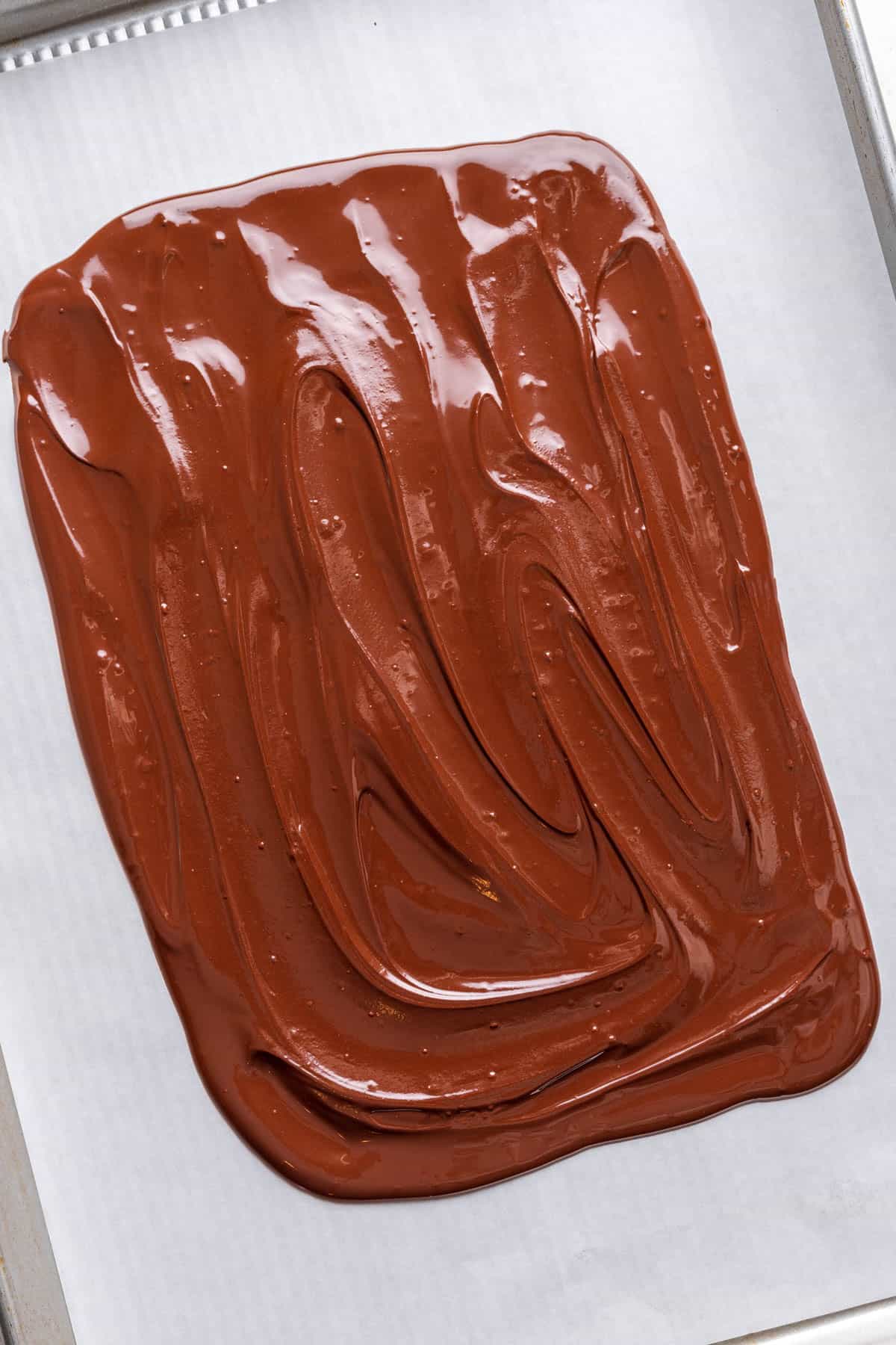 Melted semisweet chocolate smoothed into a rectangle on a parchment lined tray.