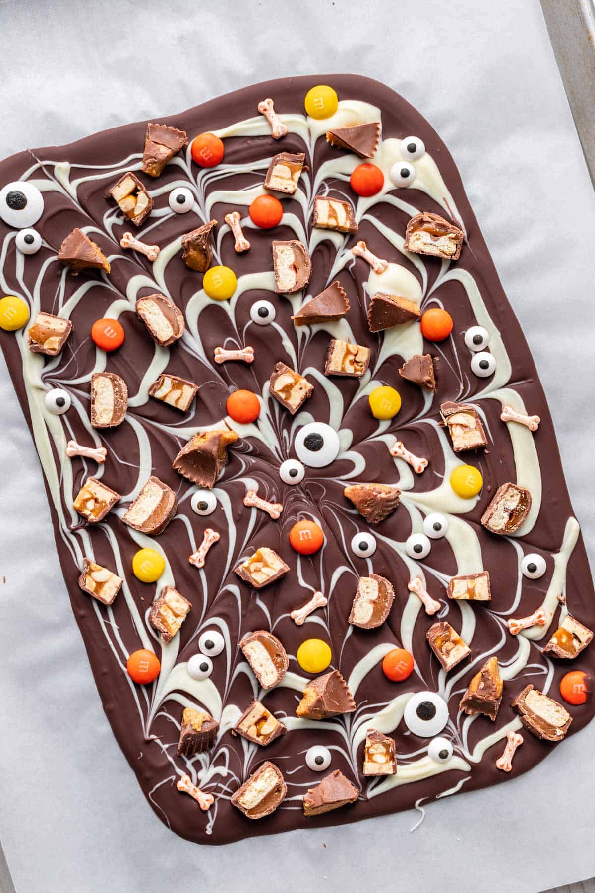 Halloween candy bark solidified on a parchment lined baking sheet.