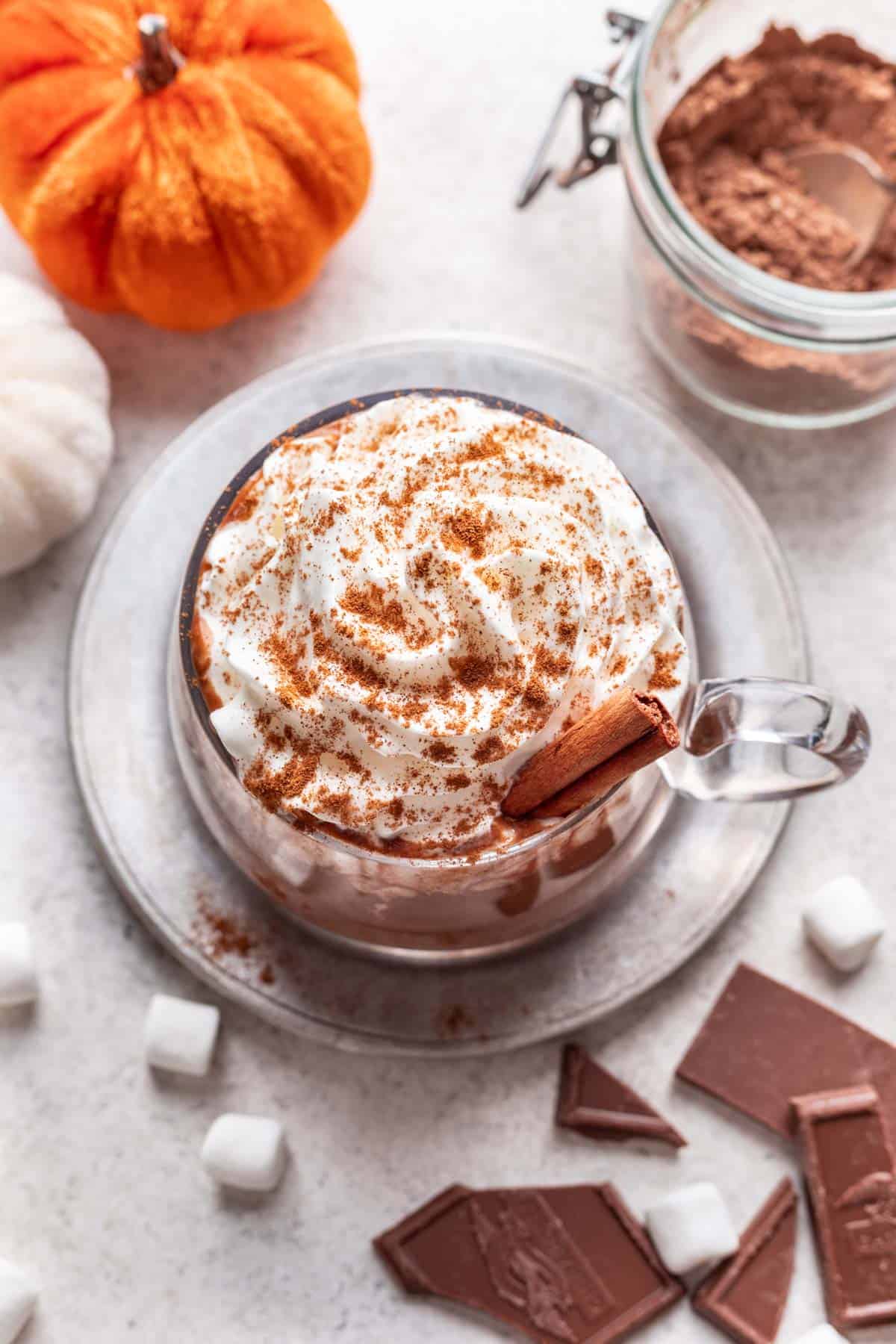 Pumpkin spice hot chocolate with whipped cream on top and a cinnamon stick.
