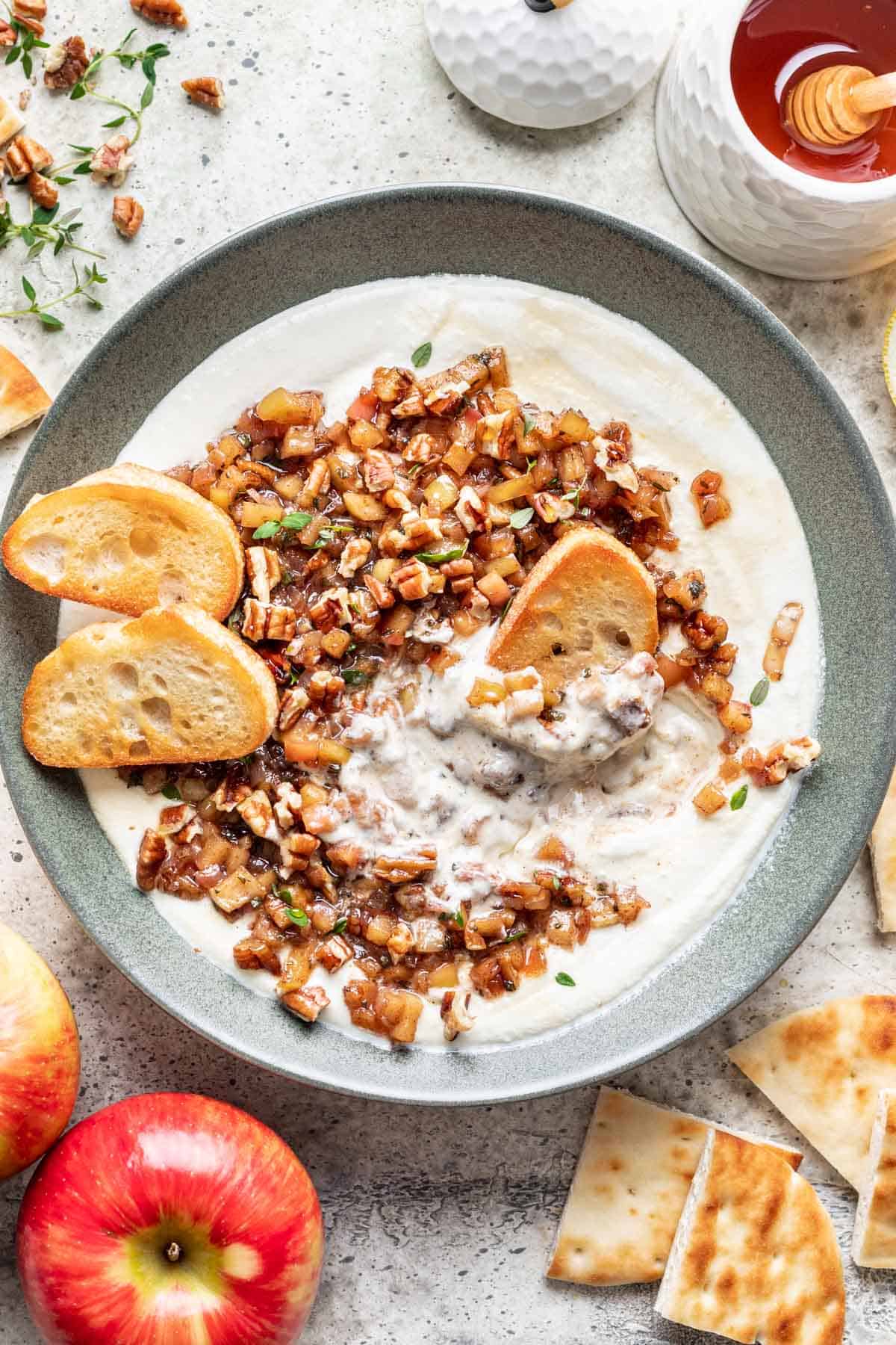 Whipped feta with apple pecan topping in a green bowl with crostini dipped in.