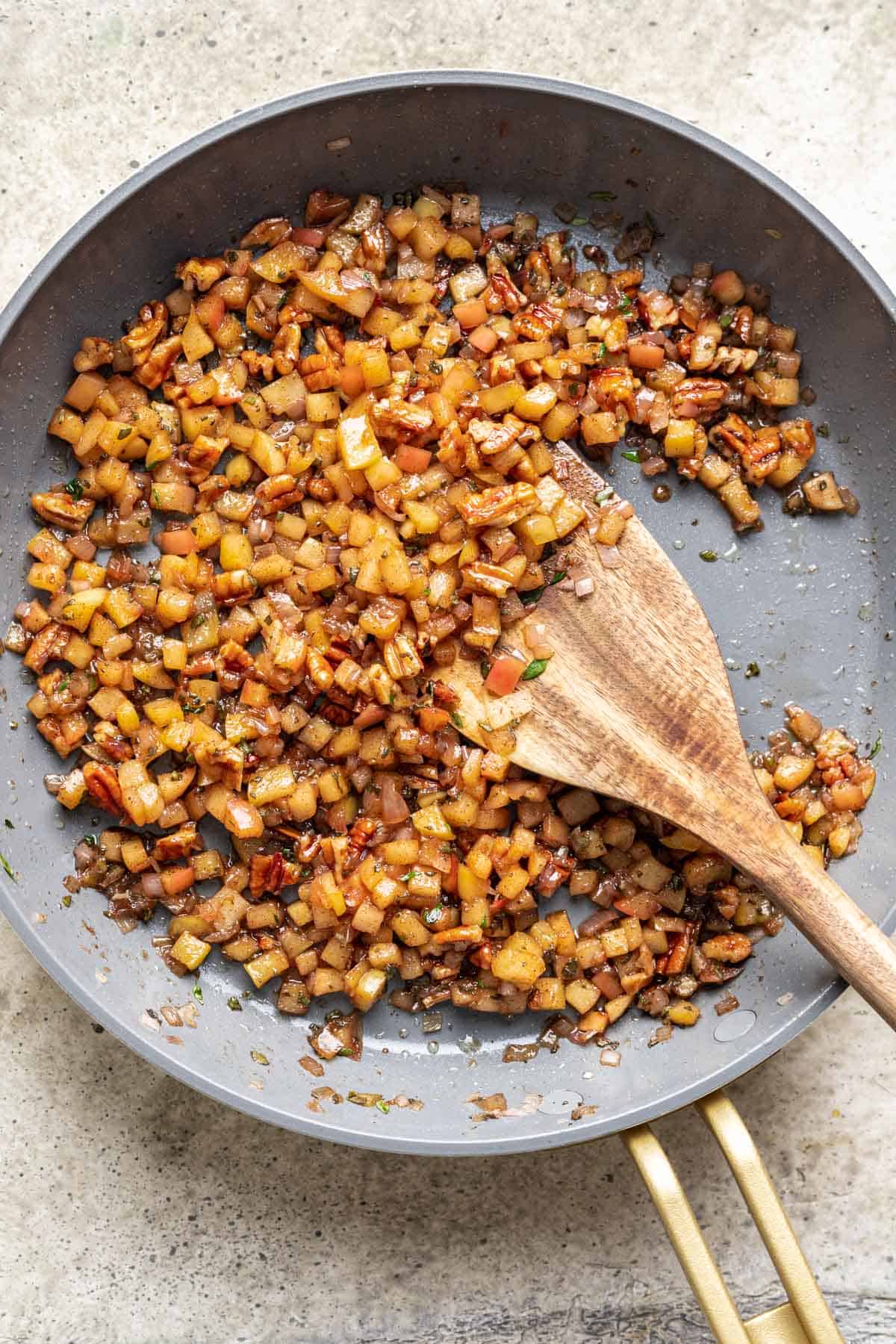 Caramelized apples, pecans, and fresh herbs in a skillet.