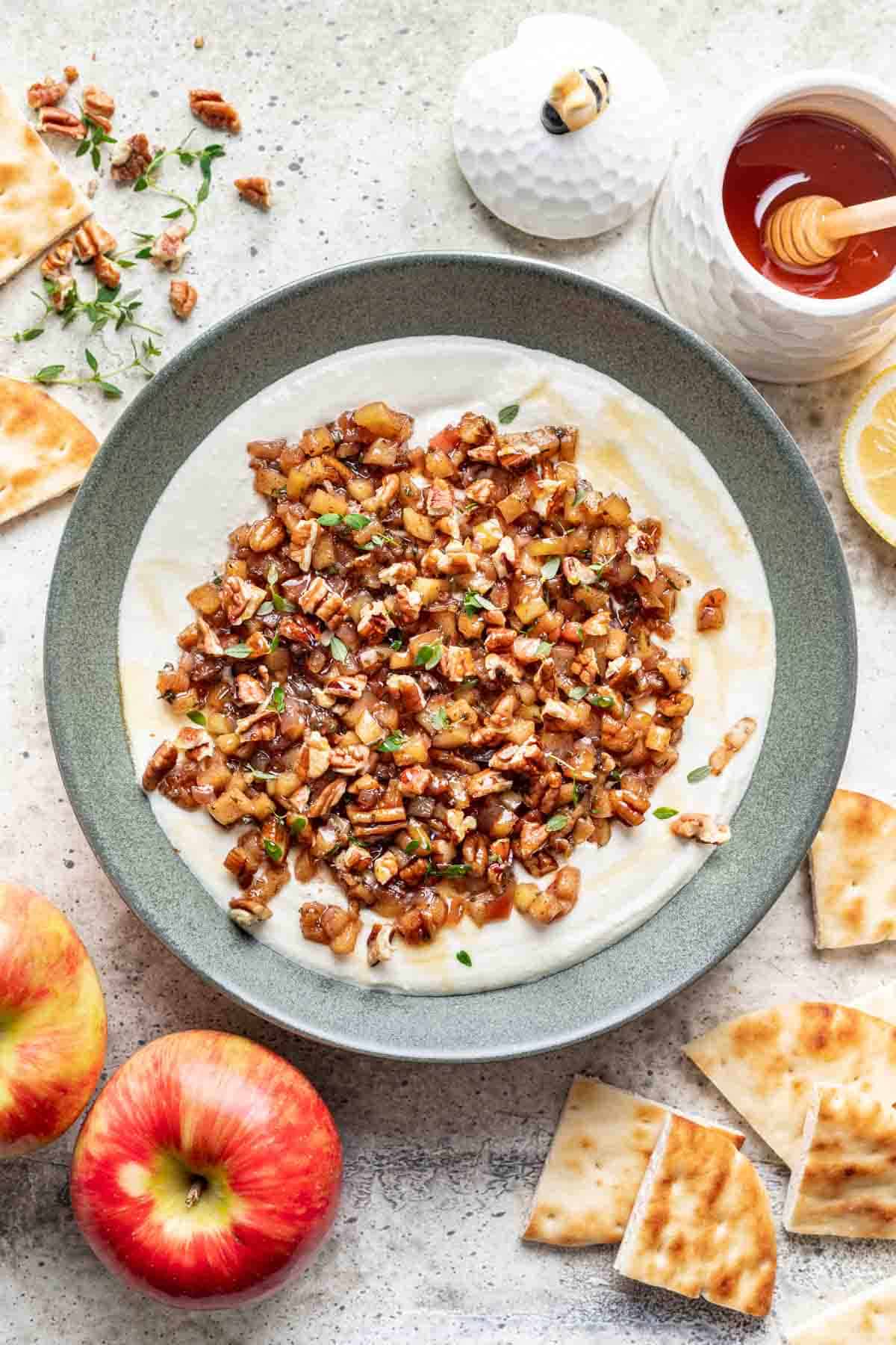 Whipped feta and apple pecan topping in a bowl with apples, honey, and pita slices around it.