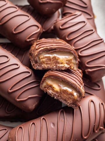 Homemade milky way bars stacked on top of each other with one split in half to show the nougat and caramel inside.