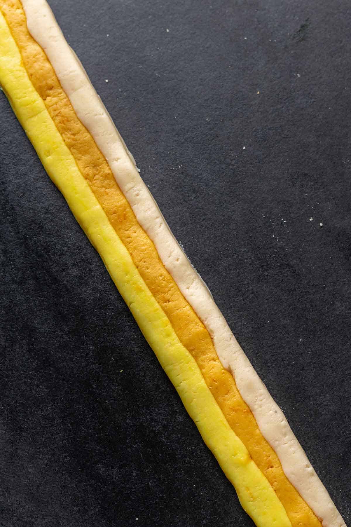A long strip of candy corn dough with white dough on top, orange in the middle, and yellow on bottom.