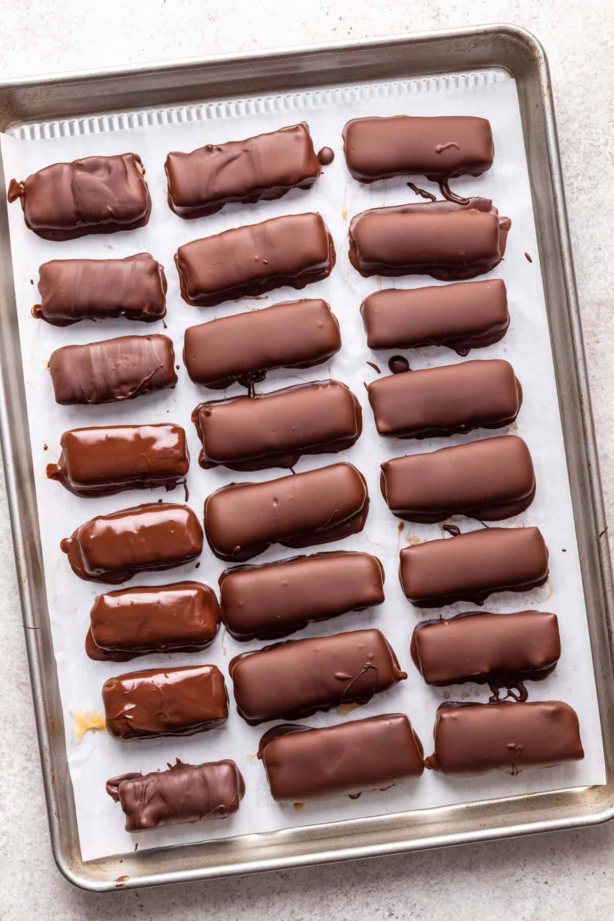 Homemade milky way bars coated in melted chocolate on a baking sheet.