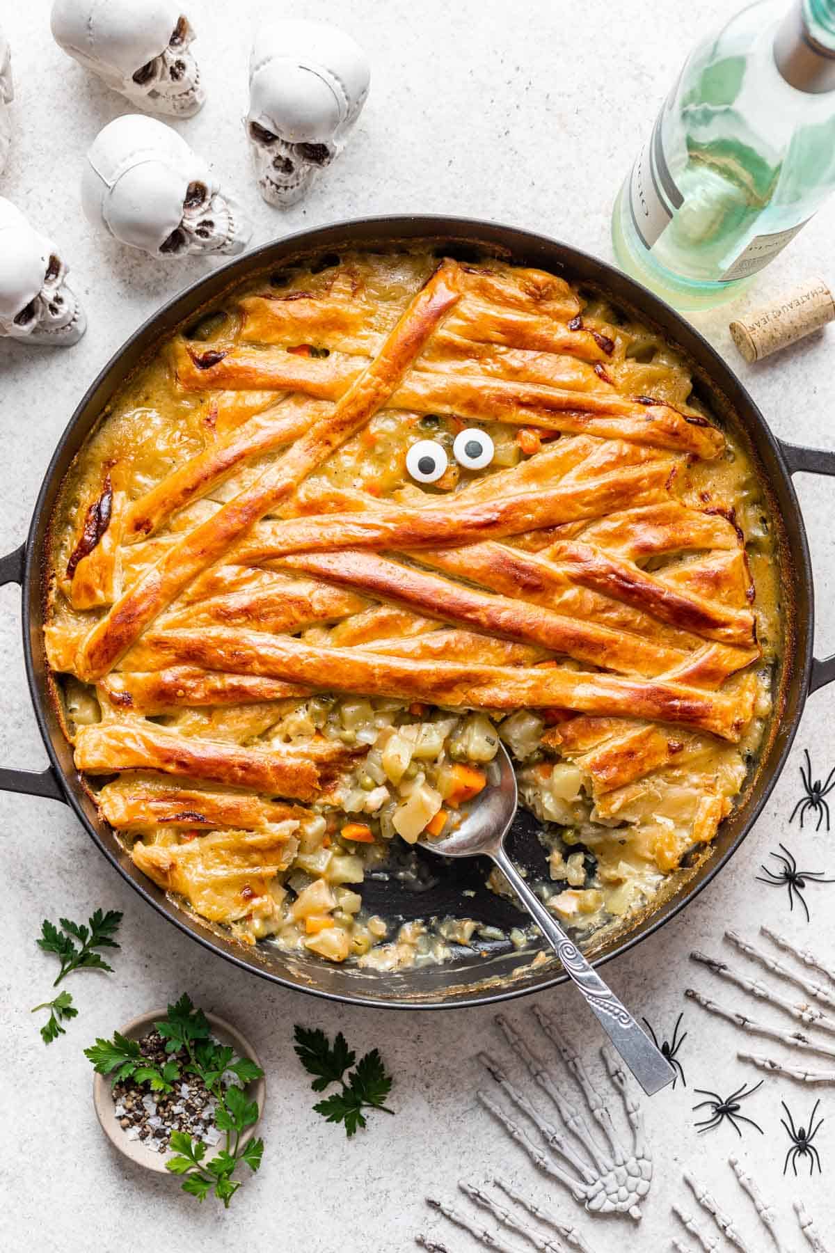 Mummy chicken pot pie in a large skillet with a spoon scooping some of the filling out.