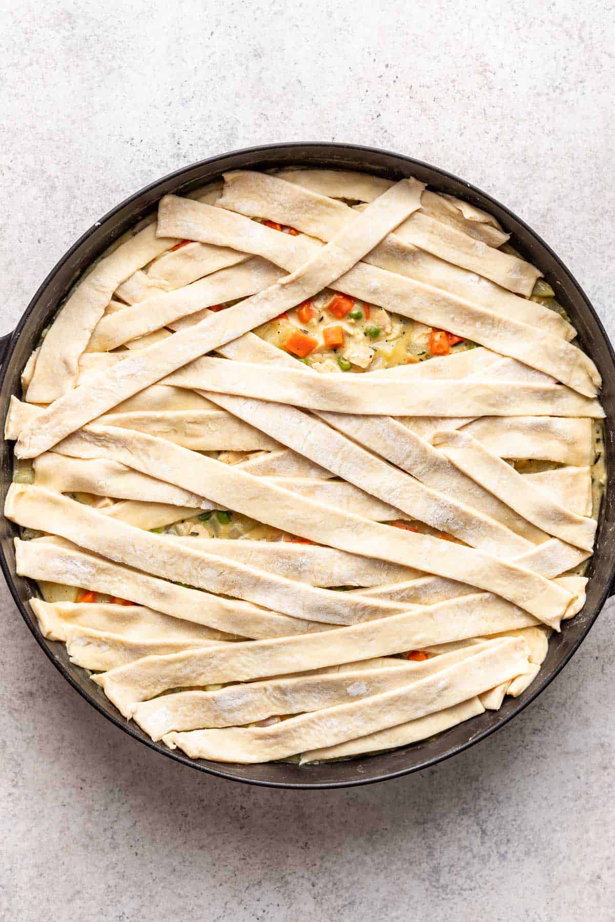 Raw puff pastry strips on top of the veggies and sauce in the skillet.