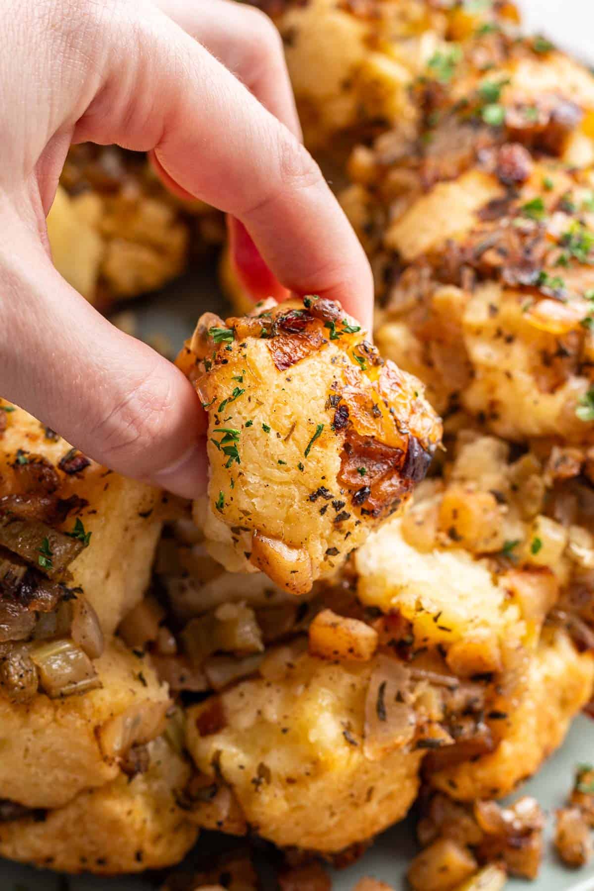 A hand picking out a piece of monkey bread from the rest of the dish.