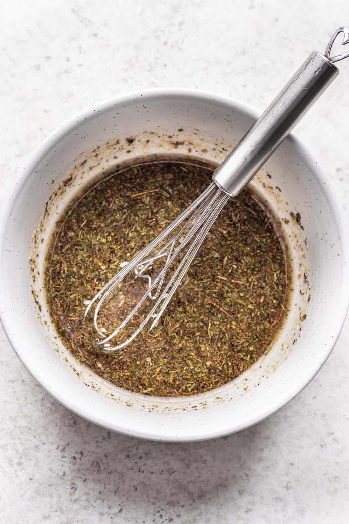 Dried herbs, seasonings, and oil whisked together in a bowl.
