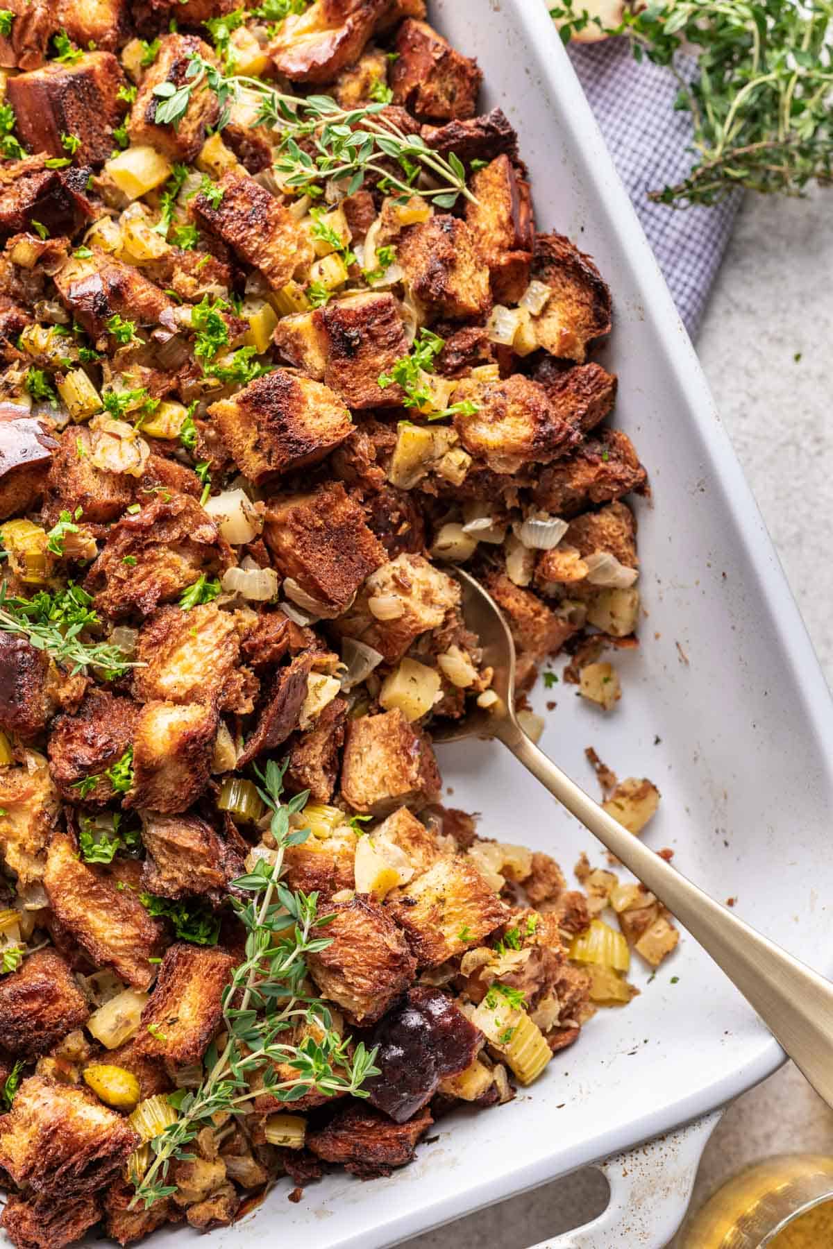 Challah bread Thanksgiving stuffing in a baking dish, with some scooped out with a gold serving spoon.