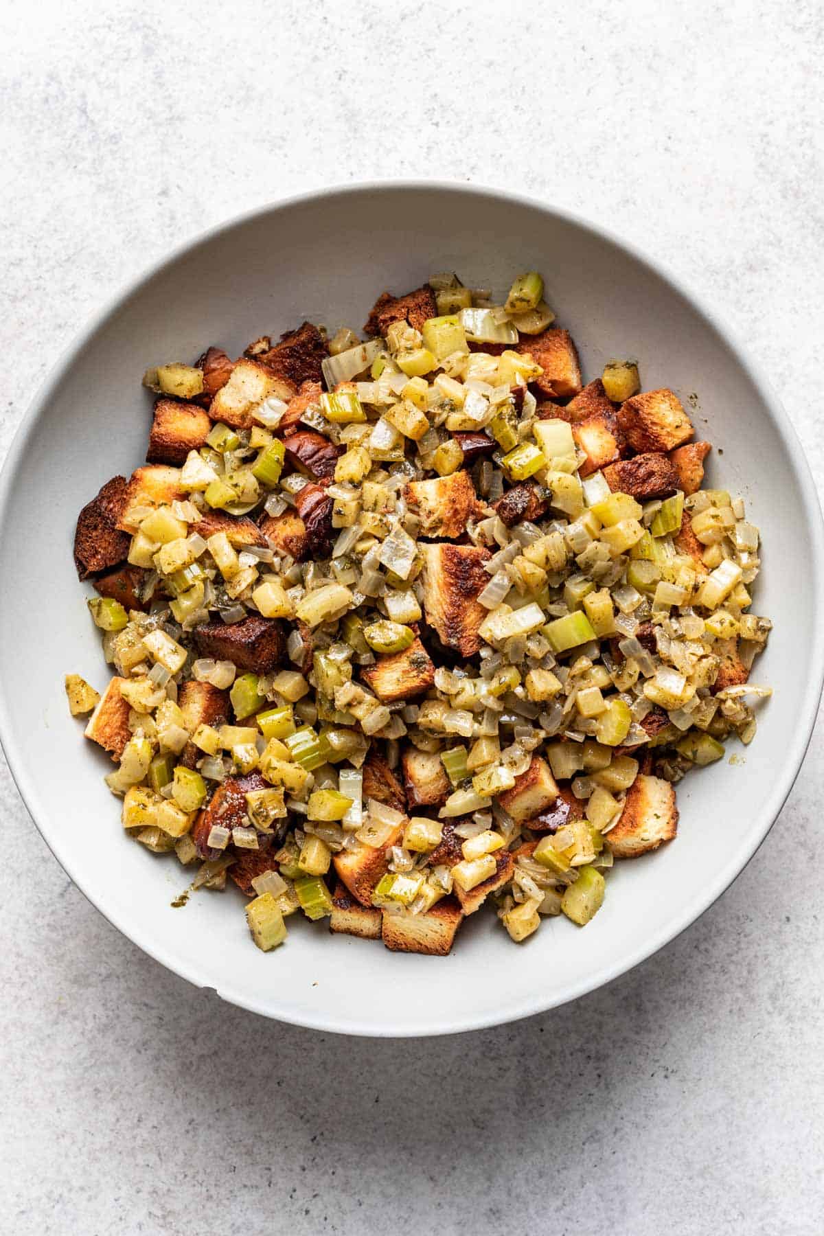 Sauteed vegetables and cubed, toasted bread in a large bowl.