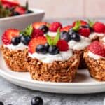 Granola cups topped with greek yogurt and fresh berries on a serving plate.