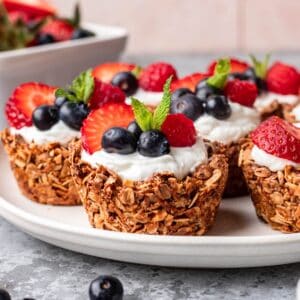 Granola cups topped with greek yogurt and fresh berries on a serving plate.