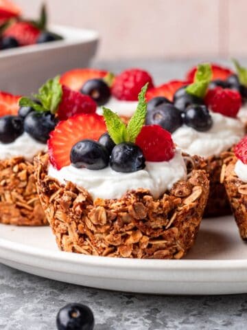 Granola cups topped with greek yogurt and fresh berries on a serving plate.