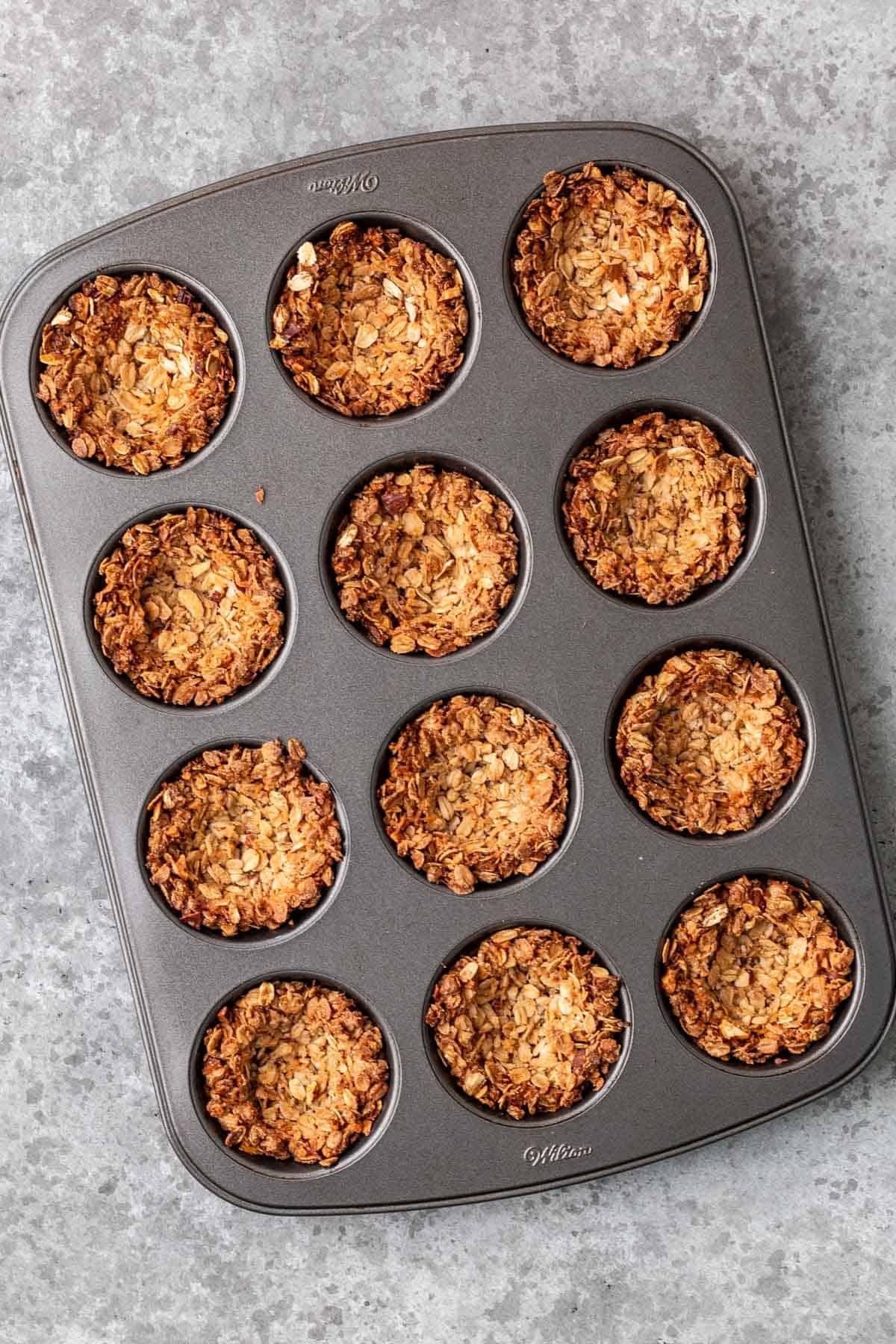 Baked golden brown granola cups in a muffin pan.