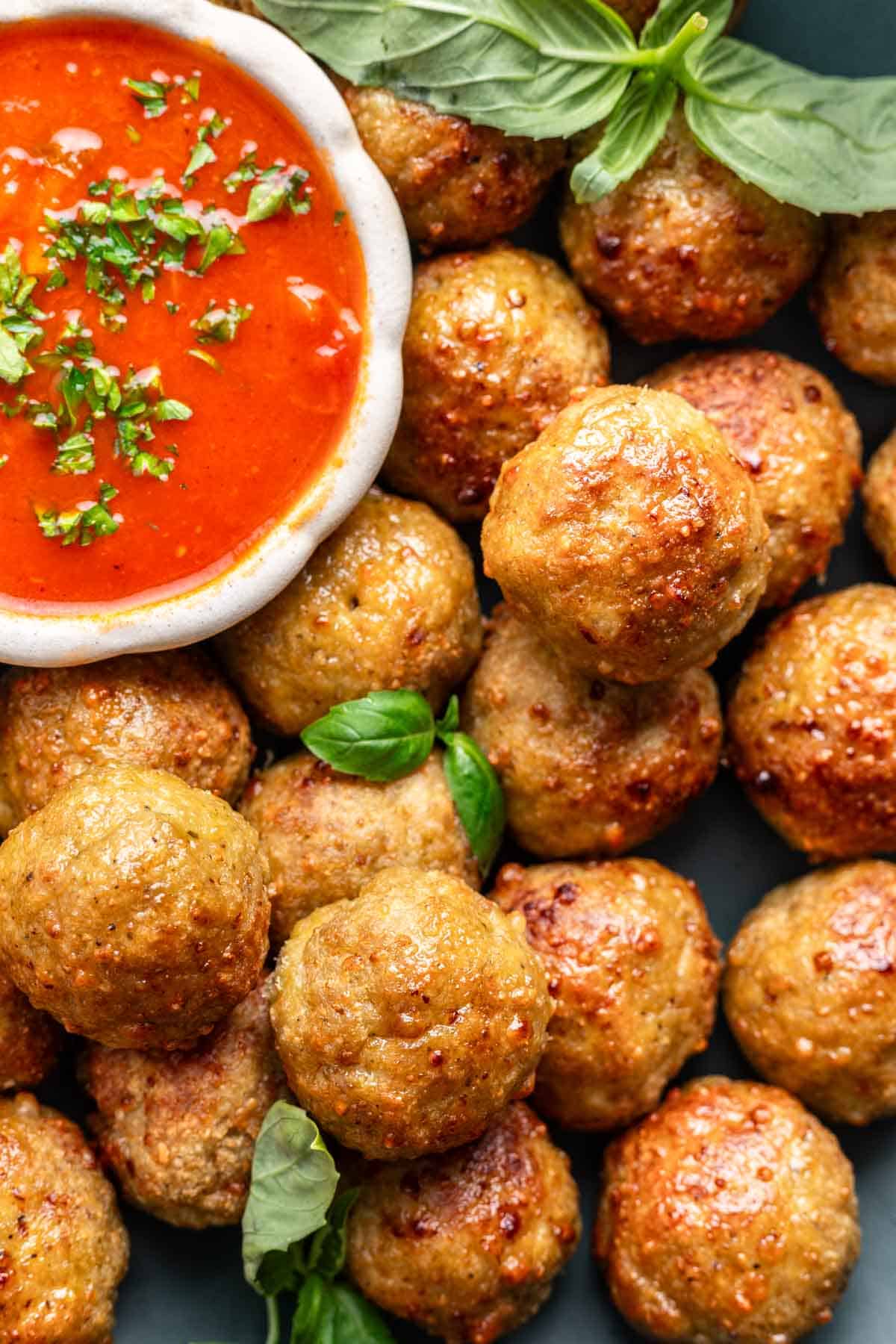 Air fryer chicken meatballs garnished with fresh basil and a side of marinara for dipping.