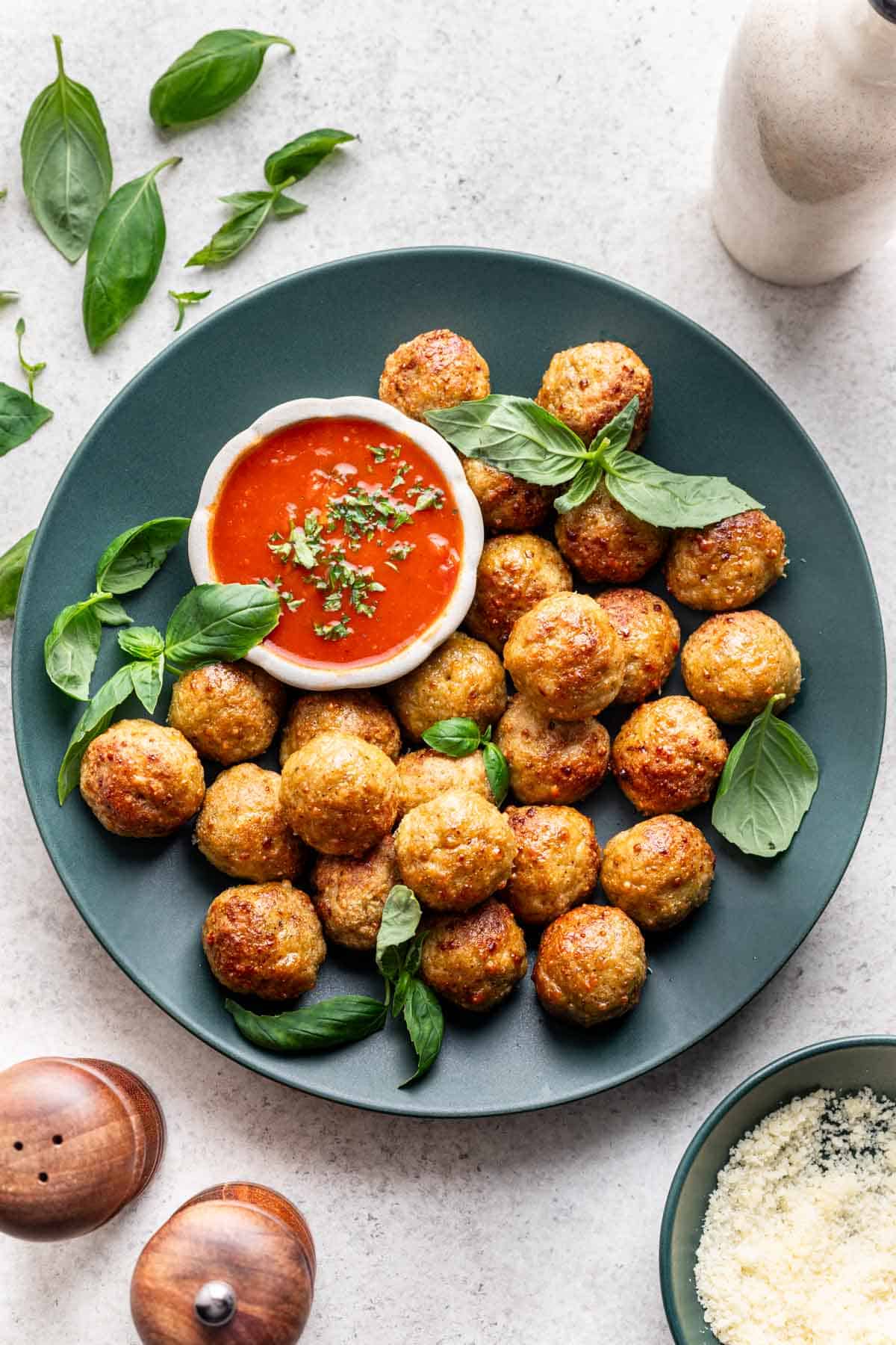 Air fryer chicken meatballs on a serving plate with marinara sauce for dipping.